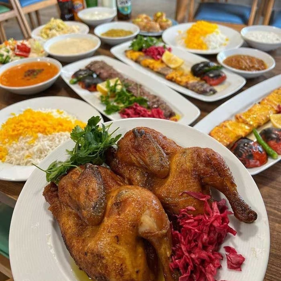 Restaurant table laden with roasted chickens, saffron rice, kebabs, colorful salads, dips, and bottled drinks.
