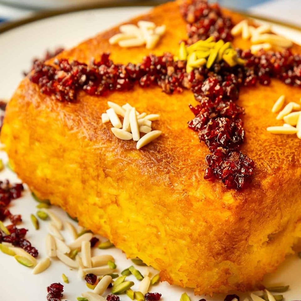 Golden Persian rice cake garnished with dried barberries, slivered almonds, and pistachios on a decorative plate.