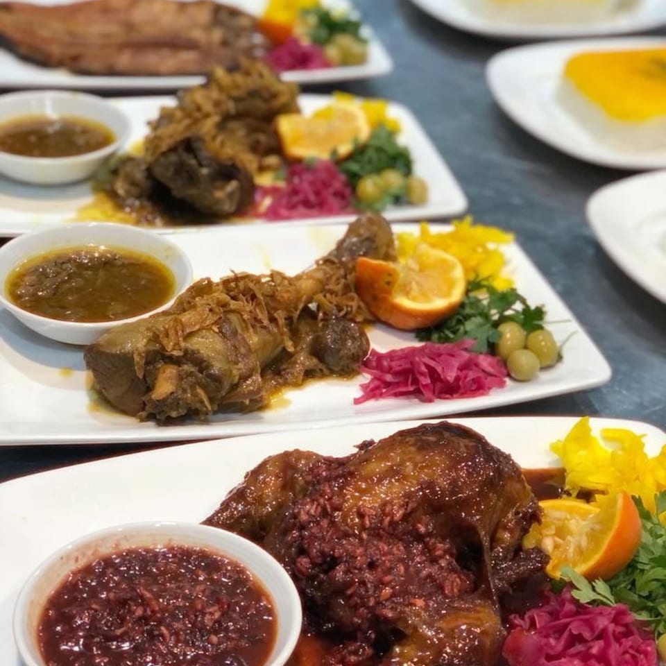Plates of roasted meats with dipping sauces, rice, pickled cabbage, vegetables, citrus, and boiled eggs arranged on a dining table.