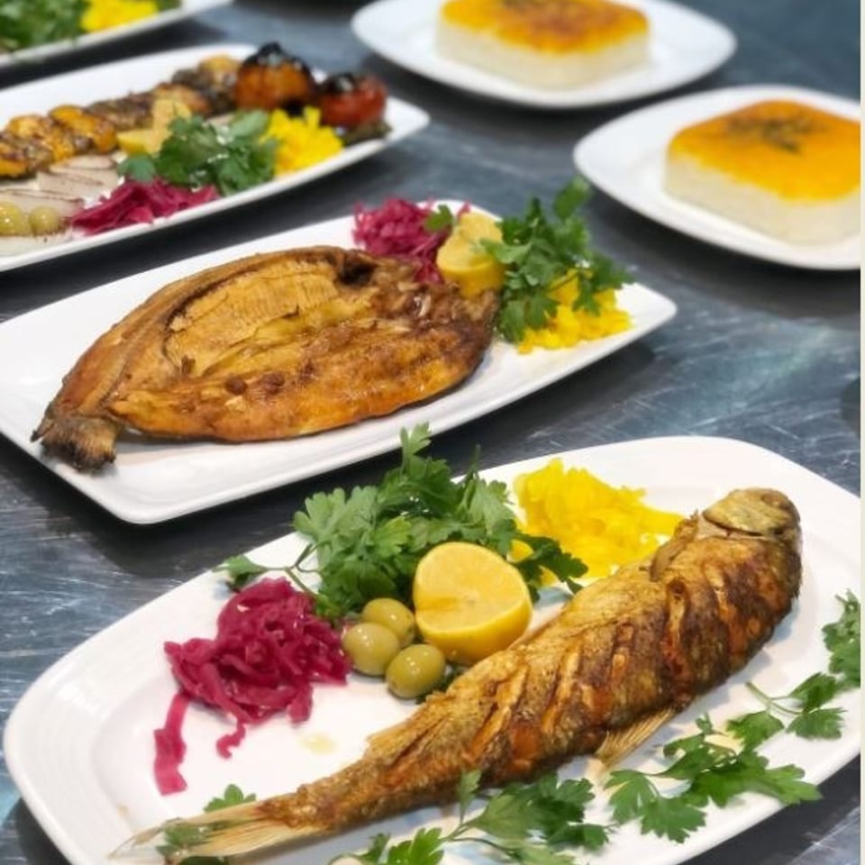 Grilled whole fish and fillets served with rice, herbs, lemon, olives, and pickled cabbage on white plates.