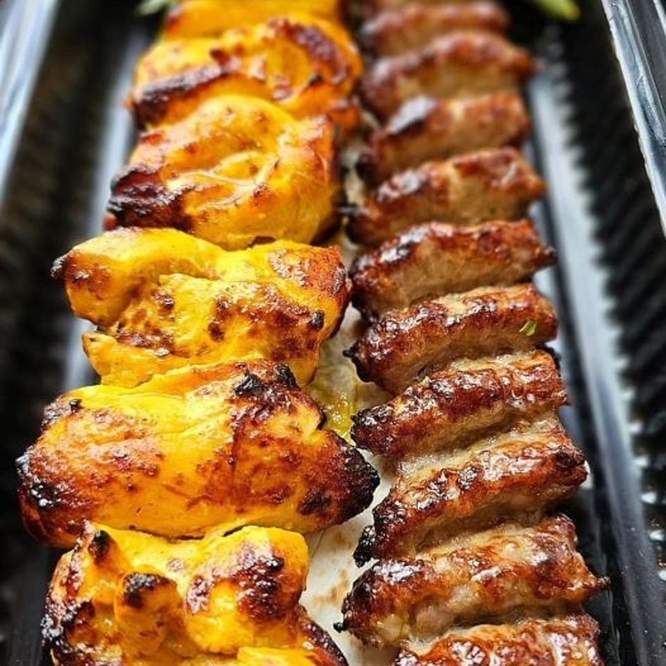 Grilled skewers of golden chicken pieces and browned sausage arranged side by side in a serving tray.