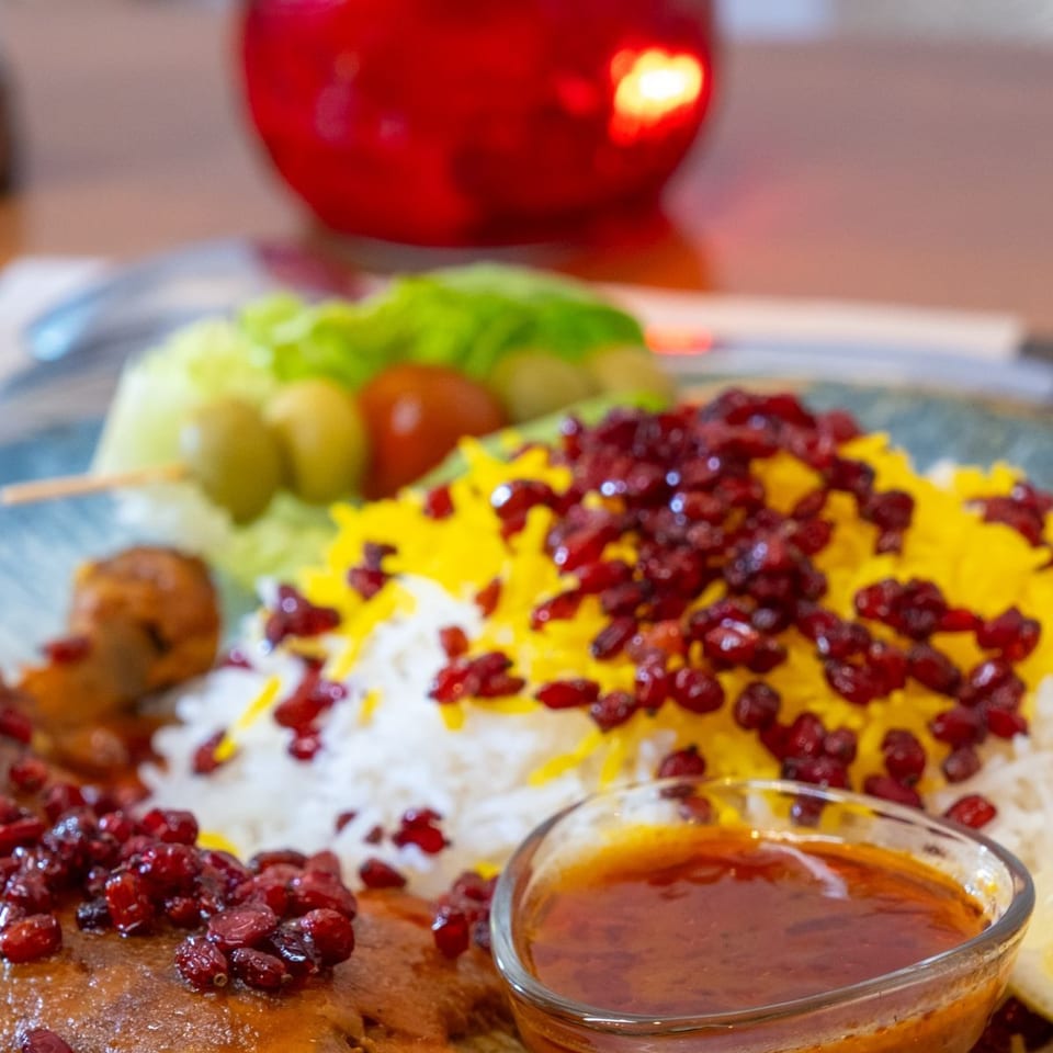 Platter of roasted chicken with saffron rice, cranberries, salad, skewered olives, and a bowl of sauce.